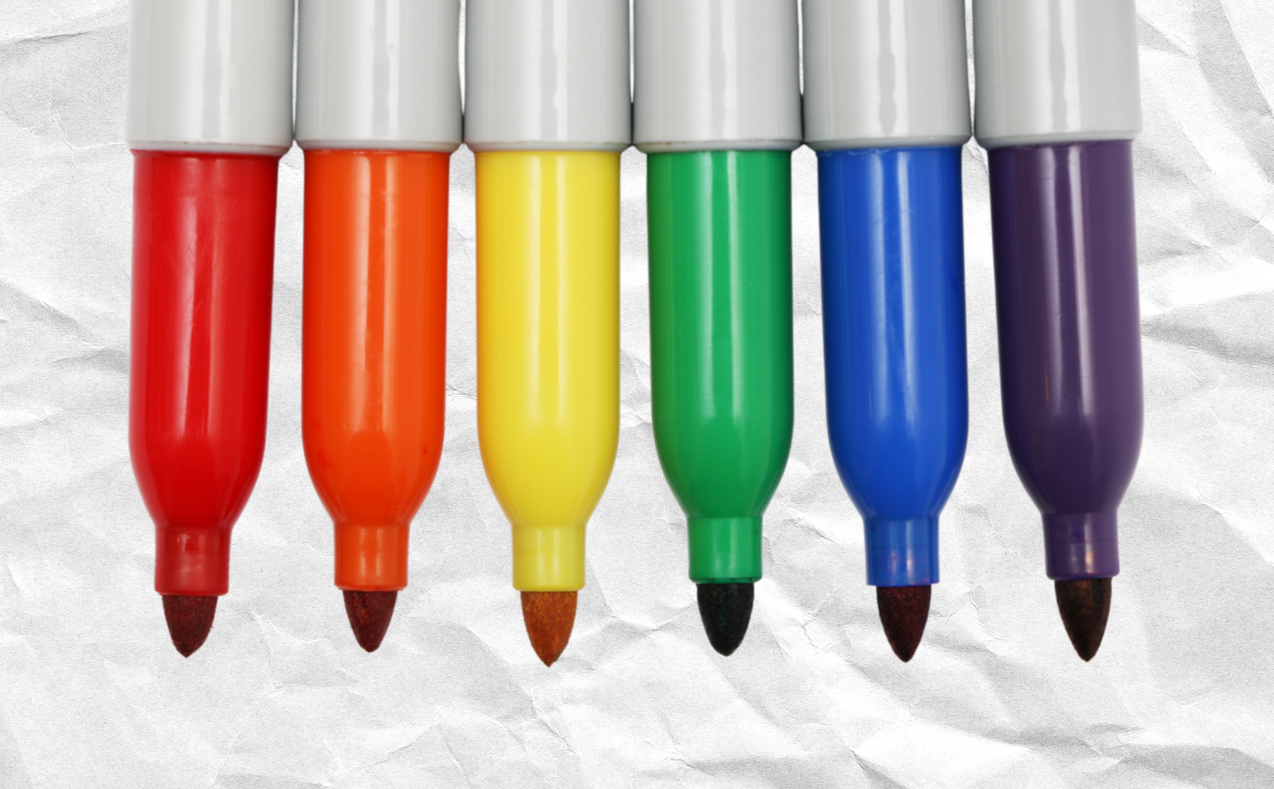 Colored sharpies in rainbow order on a background of a crumpled piece of paper